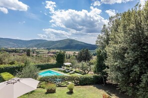 A pool area with lounge chairs and an umbrella, surrounded by greenery and hills in the background. - Tenuta Sagherina 8 in Metelliano (Cortona)
