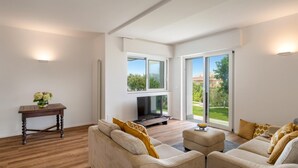 A spacious living room with a sofa set, a coffee table, and a TV. There are large windows providing a view of the outdoors. - Villa Scirocco 10 2 in Pieve Ligure (Pieve Ligure)