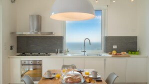 A modern kitchen with a gas stove, a stainless steel range hood, and a large window overlooking the sea. - Villa Scirocco 10 2 in Pieve Ligure (Pieve Ligure)
