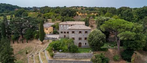 Un edificio de piedra con varias ventanas y techo de tejas, rodeado de árboles y un pequeño jardín.