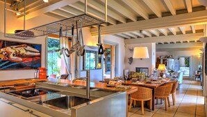 A spacious kitchen with a large island, stainless steel appliances, and a dining area with wicker chairs. - Villa Le Cave 12 in Campalto (Campiglia Marittima)