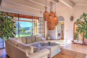 A spacious living room with a white sofa, a coffee table, and a view of the outdoors through large windows.
