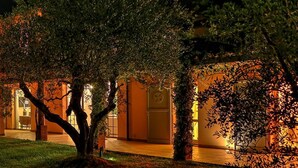 A well-lit, spacious outdoor area with a pool, seating, and a large building with multiple windows and doors. - Villa Le Cave 12 in Campalto (Campiglia Marittima)