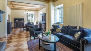 A spacious living room with a checkered floor, a dark blue sofa, a glass coffee table, and a chandelier. - Antica Villa Merelli 24 (Monte San Savino)
