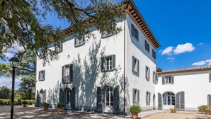 A white building with multiple windows and a gravel courtyard. - Antica Villa Merelli 24 (Monte San Savino)