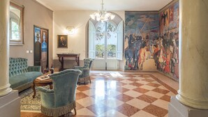 A spacious lobby with a checkered floor, a chandelier, a large mural, and a grand staircase. - Antica Villa Merelli 24 (Monte San Savino)
