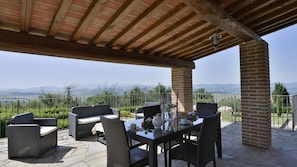 An outdoor patio with wicker furniture, a table set for dining, and a view of distant mountains. - Pi-m126-vici0at - Peruccio 4 (Volterra)