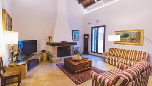 A living room with a fireplace, a sofa, a television, and a clock. - Tp-e974-ciav0at - Casale Dom 16 (Marsala)
