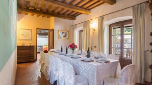 Un coin repas avec une longue table dressée pour le repas, des poutres en bois au plafond et une vue par la fenêtre.