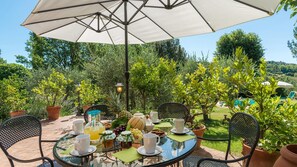 An outdoor dining area with a round glass table, metal chairs, and a large umbrella. - Fi-f398-albe0at - Villa Sorripa 6 (Montaione)