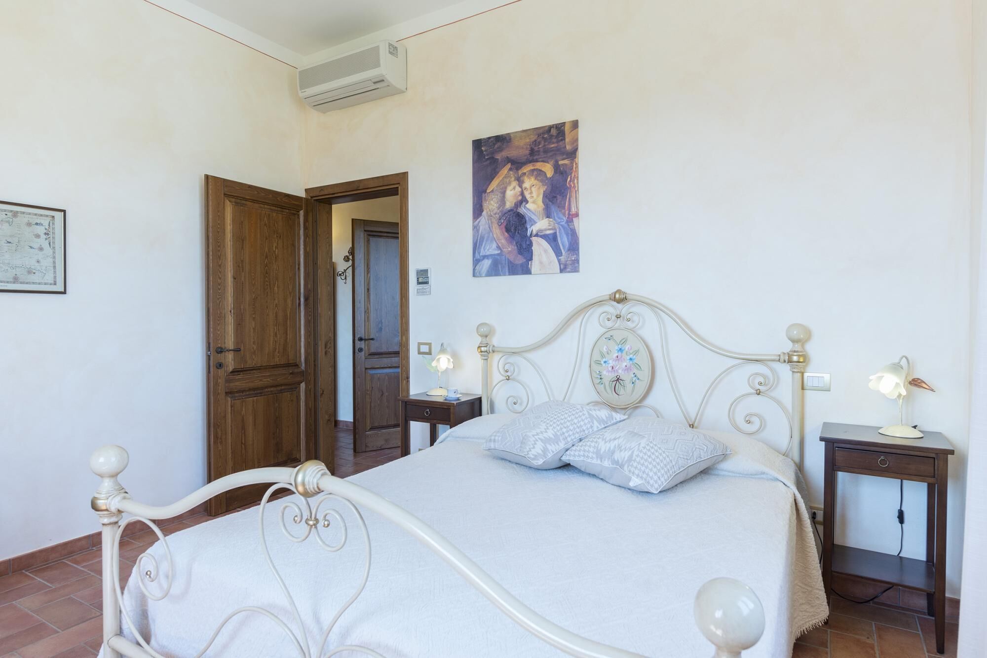 A bedroom with a bed, bedside tables, a painting, and a door.