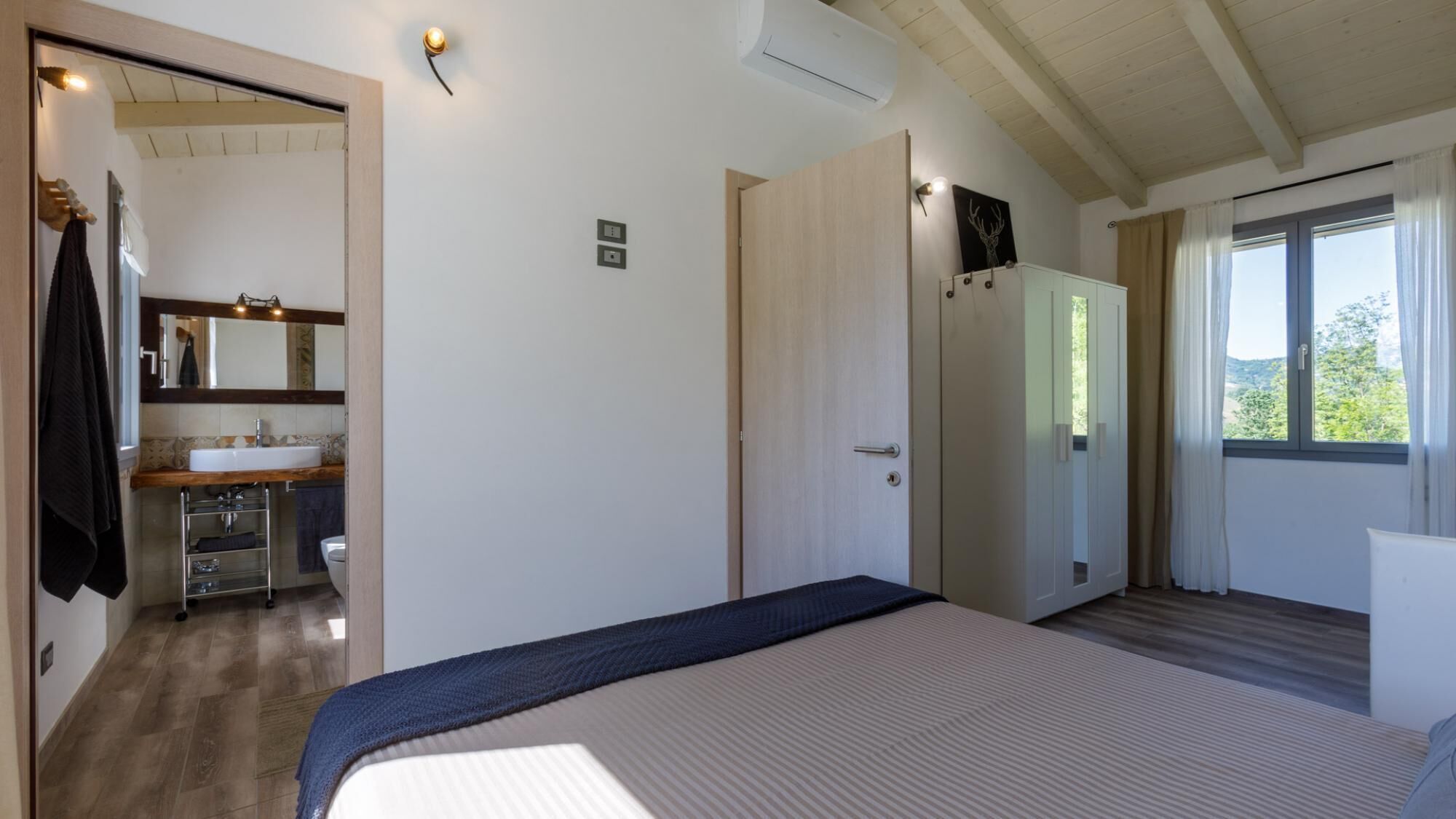 Un dormitorio con cama, un baño con lavabo y una puerta que da a otra habitación.
