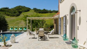 Area piscina con sedie a sdraio, una pergola e vista su una collina.