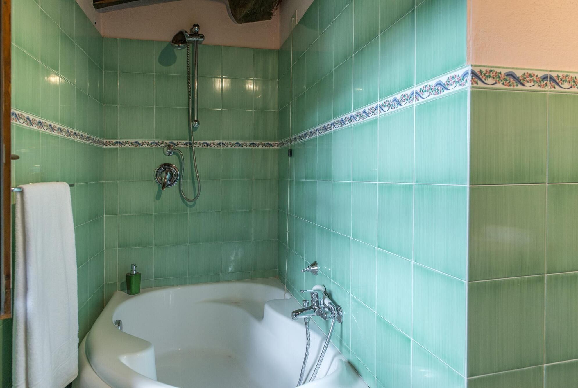 A bathroom with green tiles, a white bathtub, and a shower with a handheld showerhead.