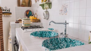 A kitchen with white tiles, a stove, two sinks with blue and white patterns, and a hanging pot rack. - Rg-e366-sp460at - Villa Ferradina 4 2 (Ispica)