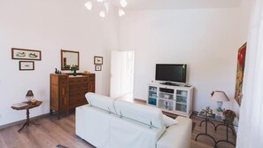 A living room with a white sofa, wooden dresser, television on a cabinet, and a lamp on a side table.