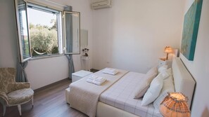 A bedroom with a bed, a chair, a bedside table, a lamp, and a window with curtains.