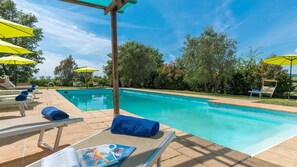 A swimming pool with lounge chairs and umbrellas, surrounded by trees.