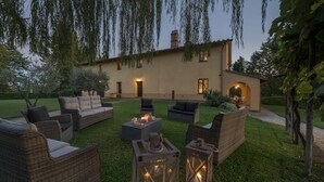 A patio area with wicker furniture, a fire pit, and a building with a lighted entrance.