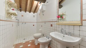Et badeværelse med hvide flisemure, trælofter, et toilet, et pissoir og to håndvaske.