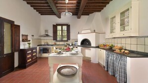 A spacious kitchen with a central island, a wood-fired oven, and a rustic ceiling.