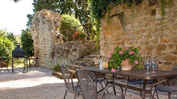 Un espace extérieur aménagé pour les repas, avec des murs en pierre, un barbecue et une table pour deux personnes, ainsi que des chaises.