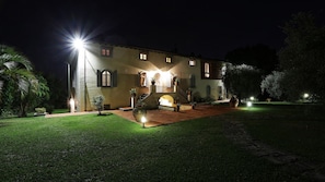 A well-lit, two-story building with a central staircase, surrounded by a manicured lawn and potted plants.