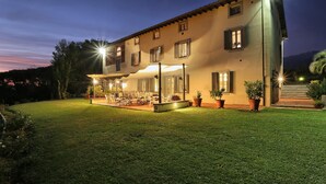 A two-story house with a covered patio area, potted plants, and a well-maintained lawn. - Lu-b648-capa0at - Villa Alida 12 (Capannori)