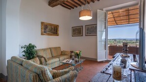 A living room with a sofa, a coffee table, and a view of the countryside through a large window.