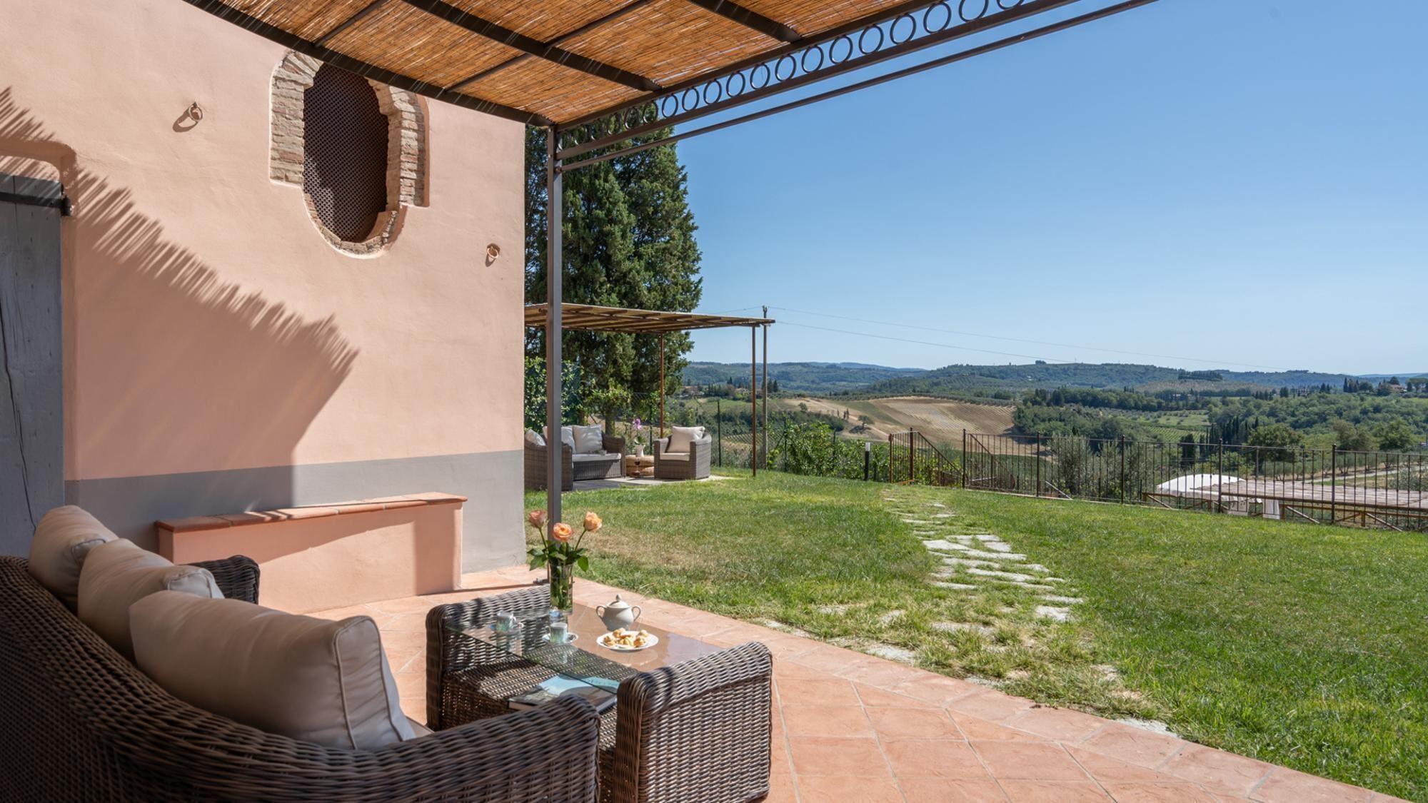 Un patio con mobiliario de mimbre, una mesa con tetera y vistas a un viñedo.