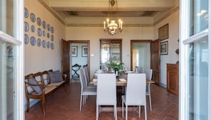 Un espace repas comprenant une longue table, des chaises, un lustre et un mur décoré d’assiettes.