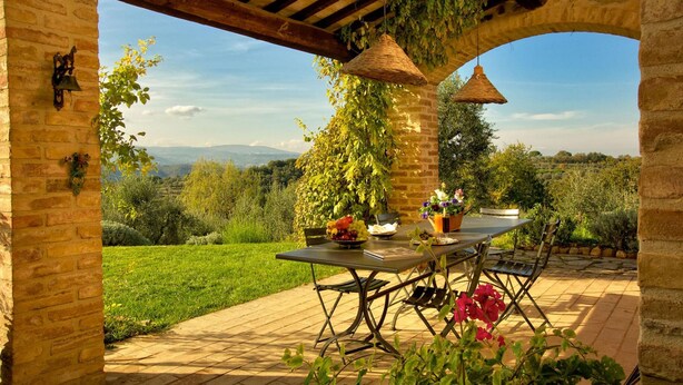 Een terras buiten, met een tafel en stoelen, omgeven door groen en uitzicht op het landschap.