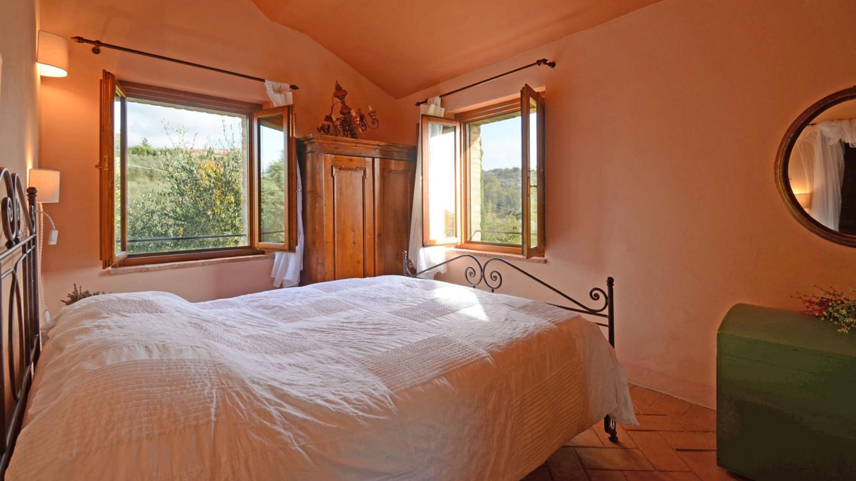 Ein Schlafzimmer mit einem Bett, zwei Fenstern, einem Spiegel und einer grünen Bank.