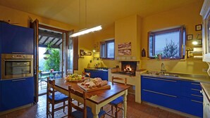 Een keuken met blauwe kastjes, een inbouwoven, een eettafel met stoelen en een open haard.
