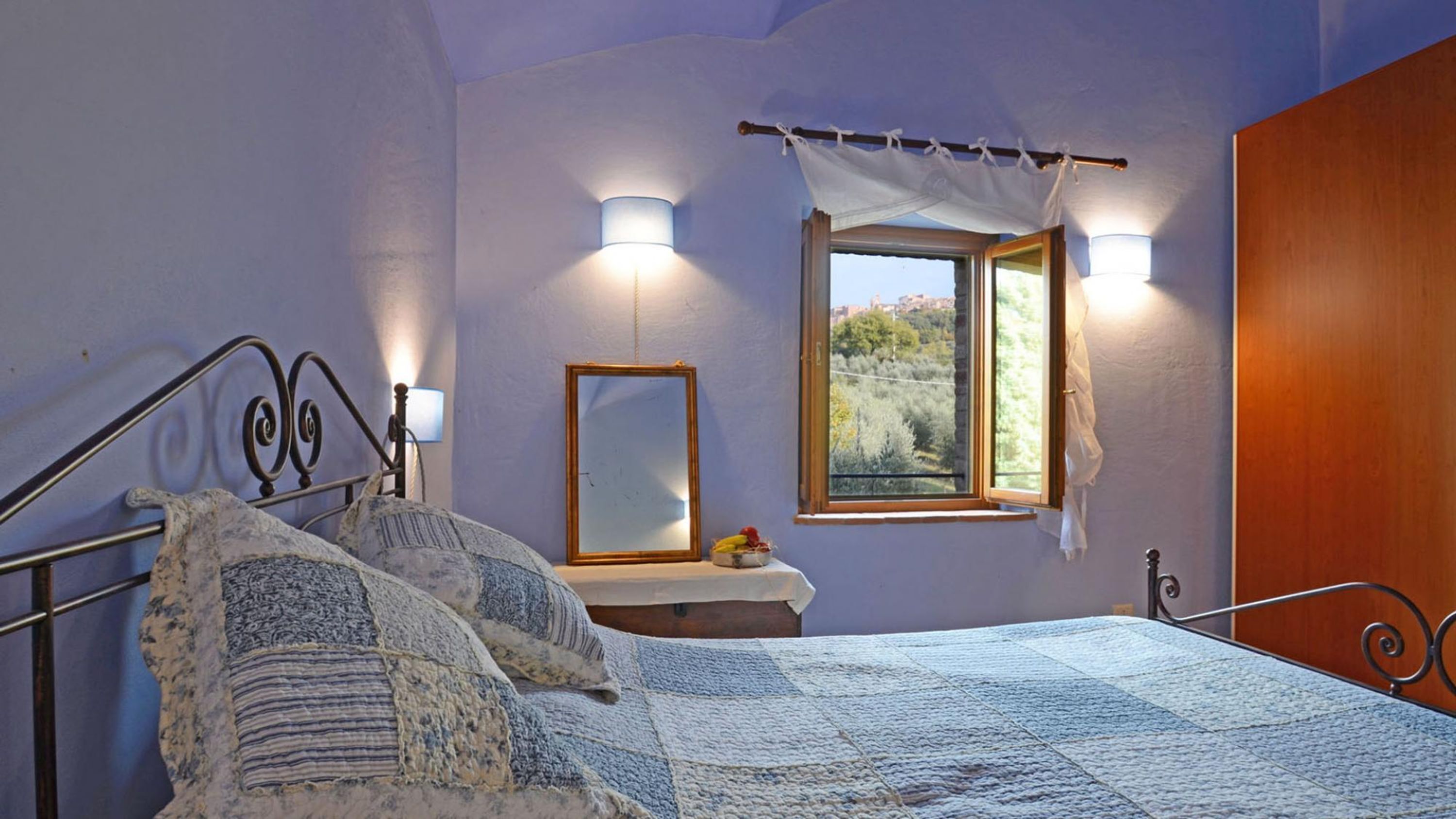 Quarto com cama, mesa de cabeceira, abajur, janela e vista para o exterior.