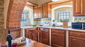 A kitchen with wooden cabinets, a brick wall, a window with a view, and a countertop with a microwave and a coffee maker. - Ar-f628-mssa0at - Villa Pucci 12 (Monte San Savino)