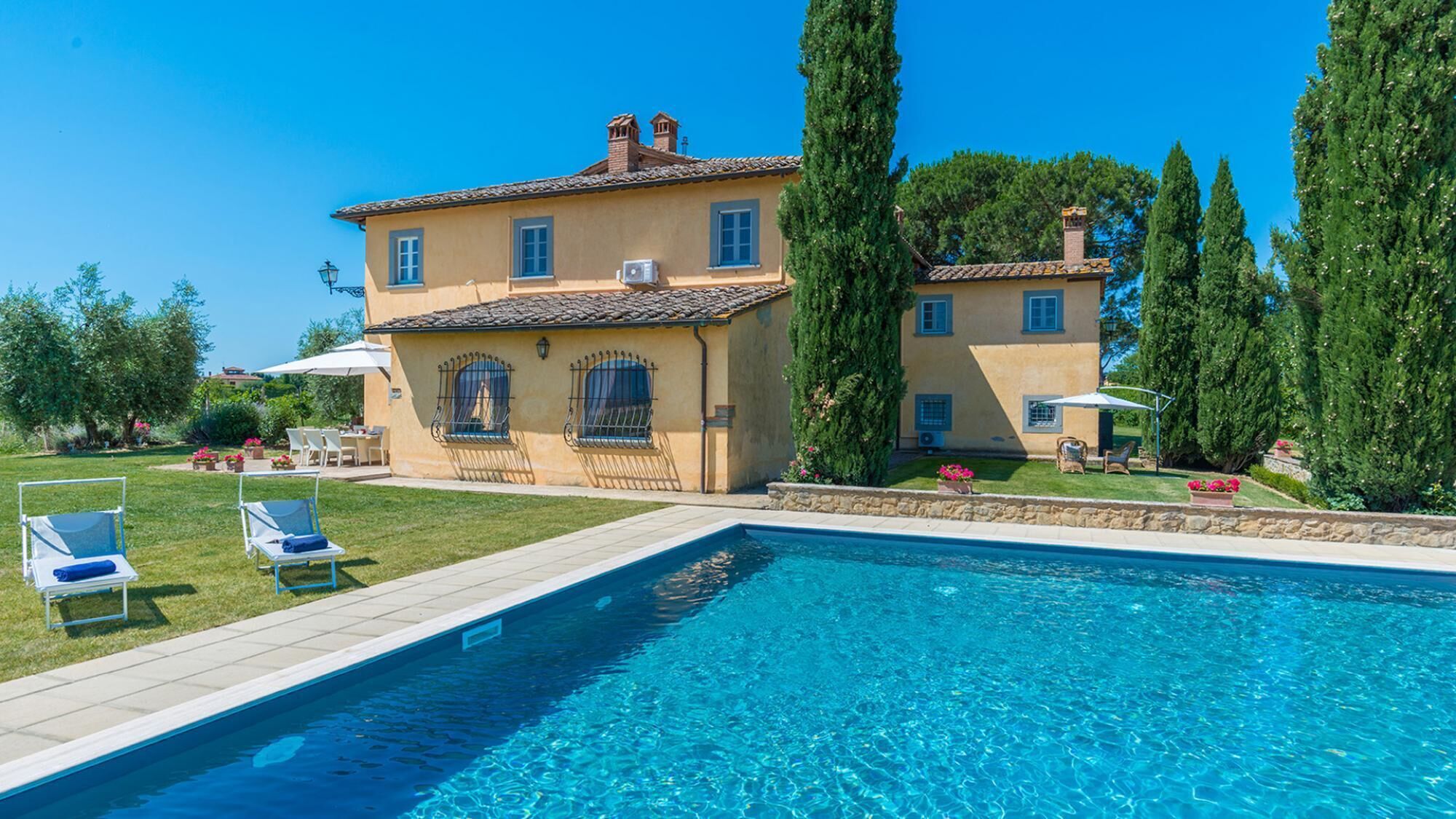 Una casa de dos pisos con piscina, mobiliario exterior y un jardín bien cuidado.