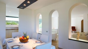 A modern dining area with a white table set for six, a fruit bowl, and a view of the outdoor garden. - Rn-h274-pini35at - Villa Sarah 10 2 (Riccione)