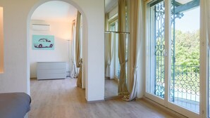 A room with a large window, a mirror, a white dresser, and a painting of a car on the wall. - Rn-h274-pini35at - Villa Sarah 10 2 (Riccione)