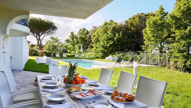 A dining table set outdoors with chairs, a pool, and greenery in the background. - Rn-h274-pini35at - Villa Sarah 10 2 (Riccione)