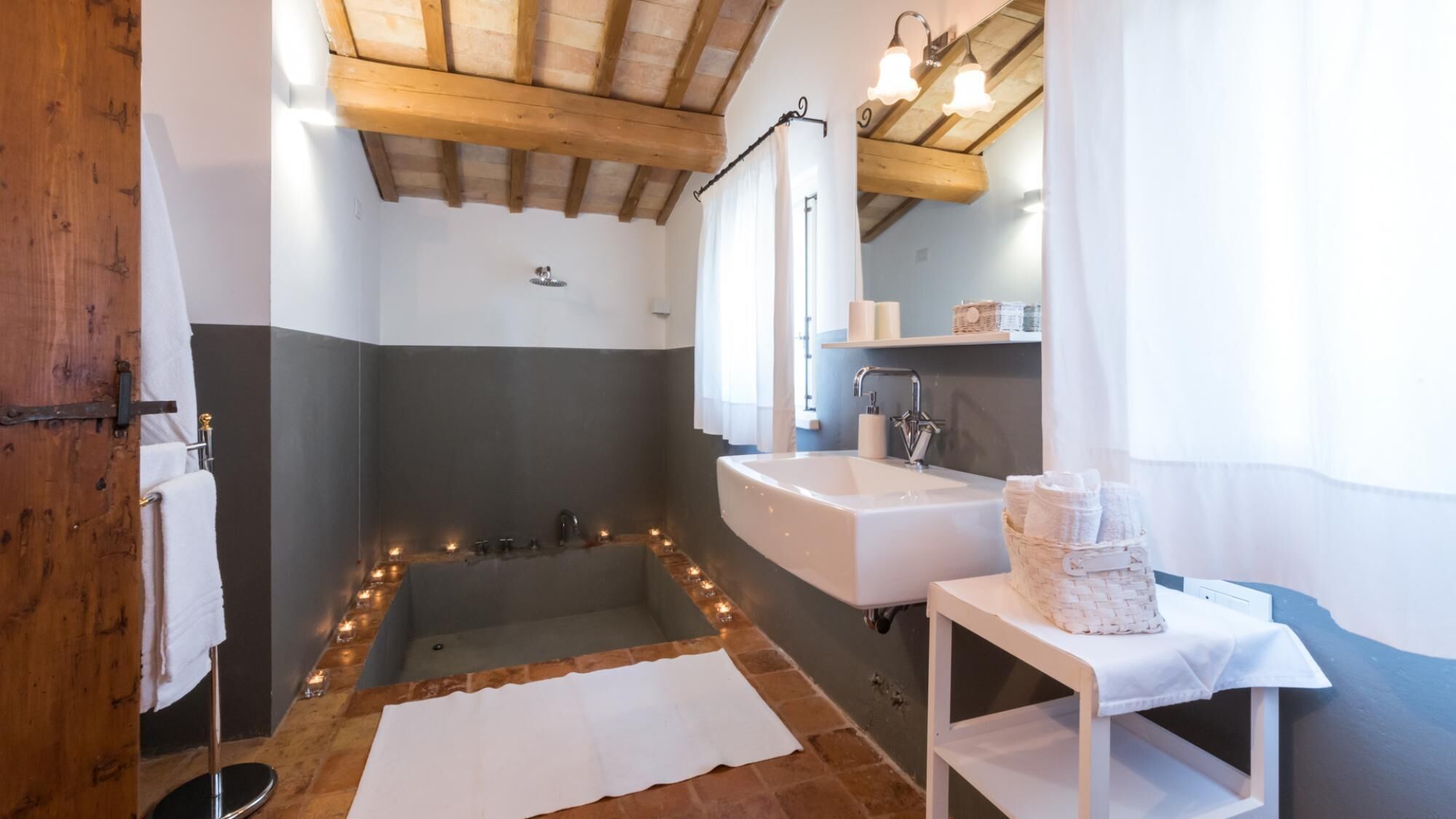 A bathroom with a bathtub, a sink, and a mirror. There are candles on the floor and a towel on the wall.