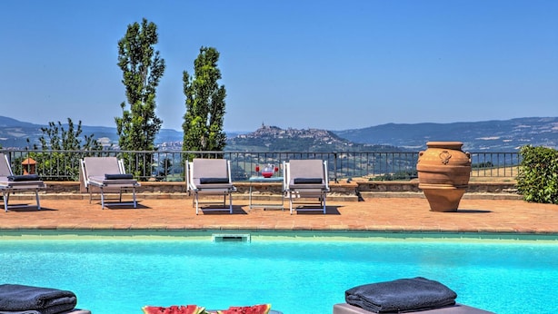A poolside area with lounge chairs, a large terracotta pot, and a view of a distant hill with a castle. - Pg-l188-todi0at - Casal Del Salice 10 (Todi)
