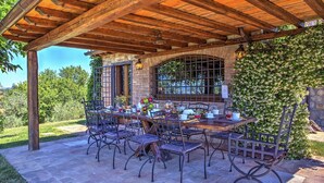 An outdoor patio with a wooden pergola, stone flooring, and metal chairs. - Pg-l188-todi0at - Casal Del Salice 10 (Todi)