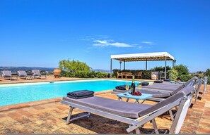 Un área junto a la piscina con sillones de descanso, una zona de estar cubierta y vistas al paisaje.