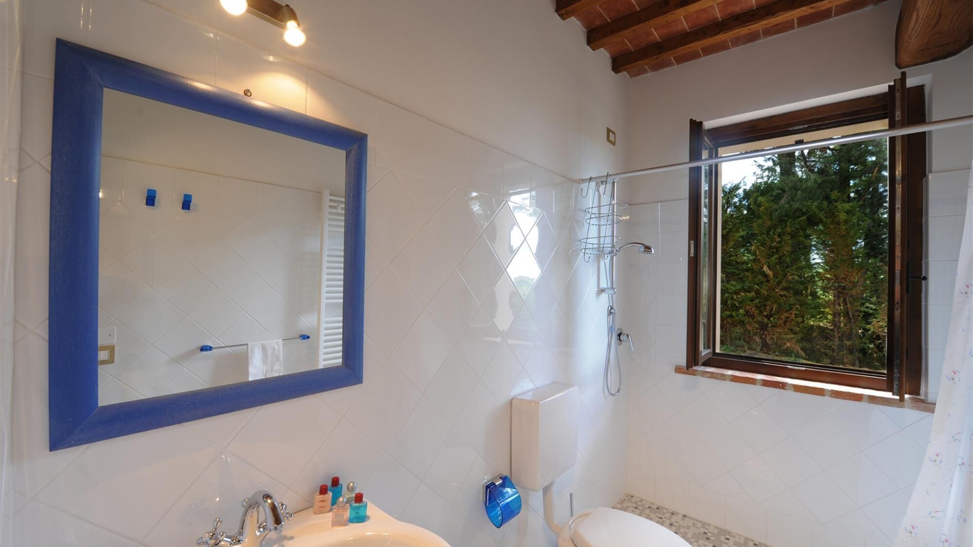 Une salle de bain moderne avec un grand miroir, une douche et une fenêtre donnant sur les arbres.