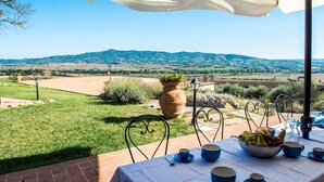 An outdoor dining area with a table set for two, surrounded by a scenic view of hills and fields.