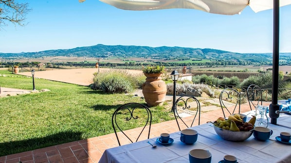 An outdoor dining area with a table set for two, surrounded by a scenic view of hills and fields.