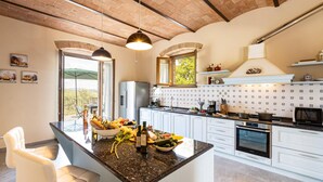 A modern kitchen with a central island, white cabinetry, a built-in oven, and a large window overlooking greenery. - Si-g752-sdto0at - Tenuta di Macericca 10 (Poggibonsi)