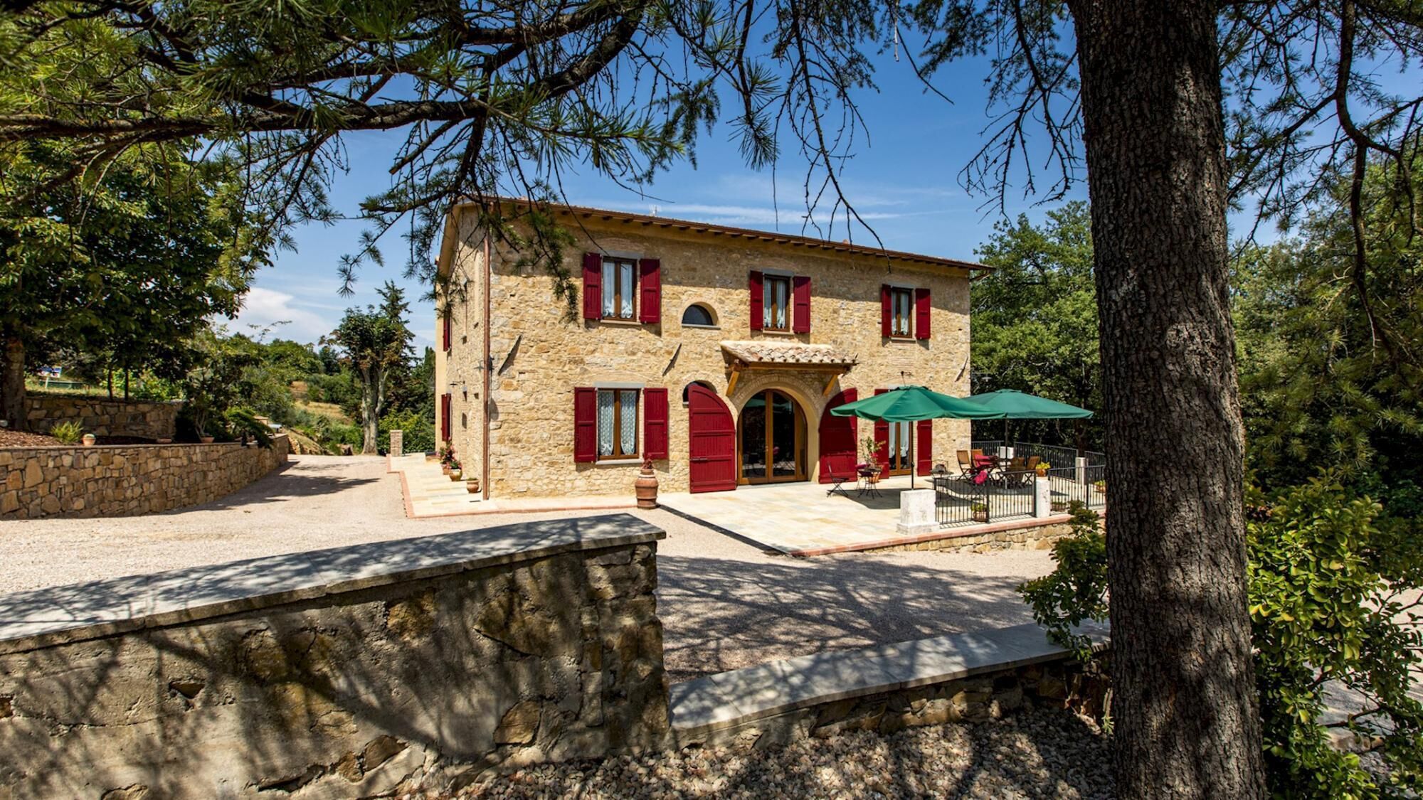 A stone building with red shutters, a patio with outdoor seating, and a stone wall in the foreground.