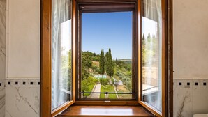A view from a room with a wooden floor and white marble walls, looking out to a garden with a pool and trees. - Si-g752-sdto0at - Tenuta di Macericca 10 (Poggibonsi)